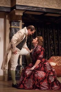 Horner in knee britches, vest and long coat and one foot perched on a sette speaks down to Lady Fidget in fancy red dress sitting on the edge of the settee
