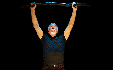 Patrick Page in All the Devils Are Here 2 Patrick Page, wearing a black t-shirt, holds the staff over his head.